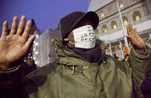 A protester holds up his hands and wears a mask with the words 